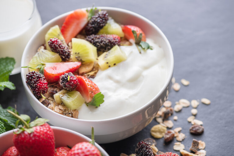 bowl of oat granola with yogurt, fresh mulberry, strawberries, kiwi mint and nuts on the black rock board.